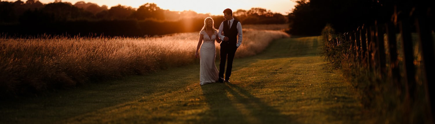 Couple walking through countryside at sunset wedding