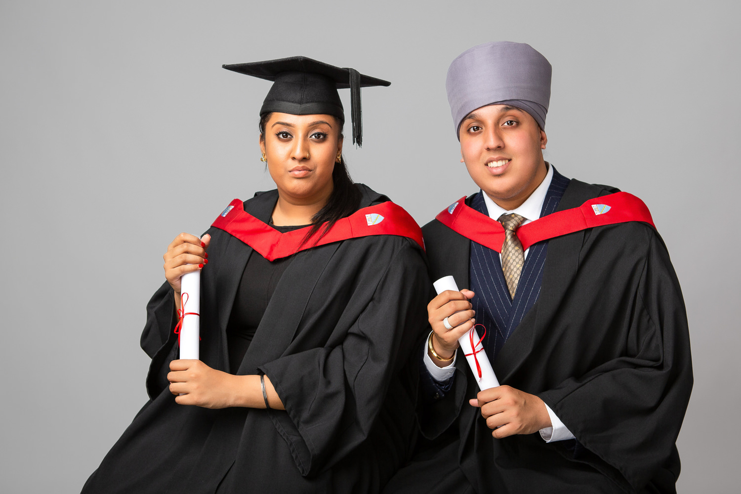 Two graduates in caps and gowns smiling.