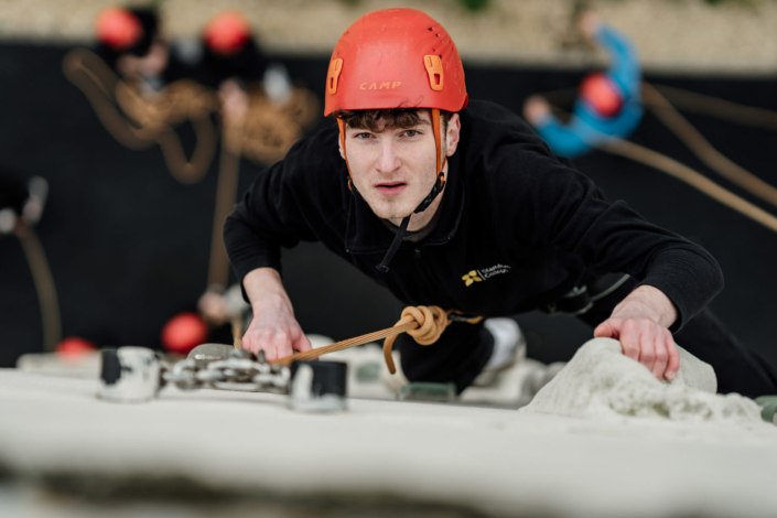 Man climbing indoor rock wall with helmet