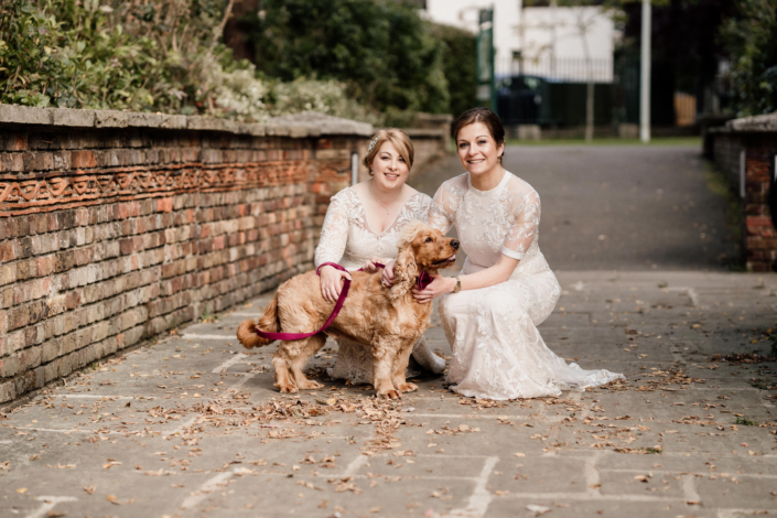 Two brides with dog in wedding dresses